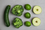 Different green vegetables and fruits on grey background, top view