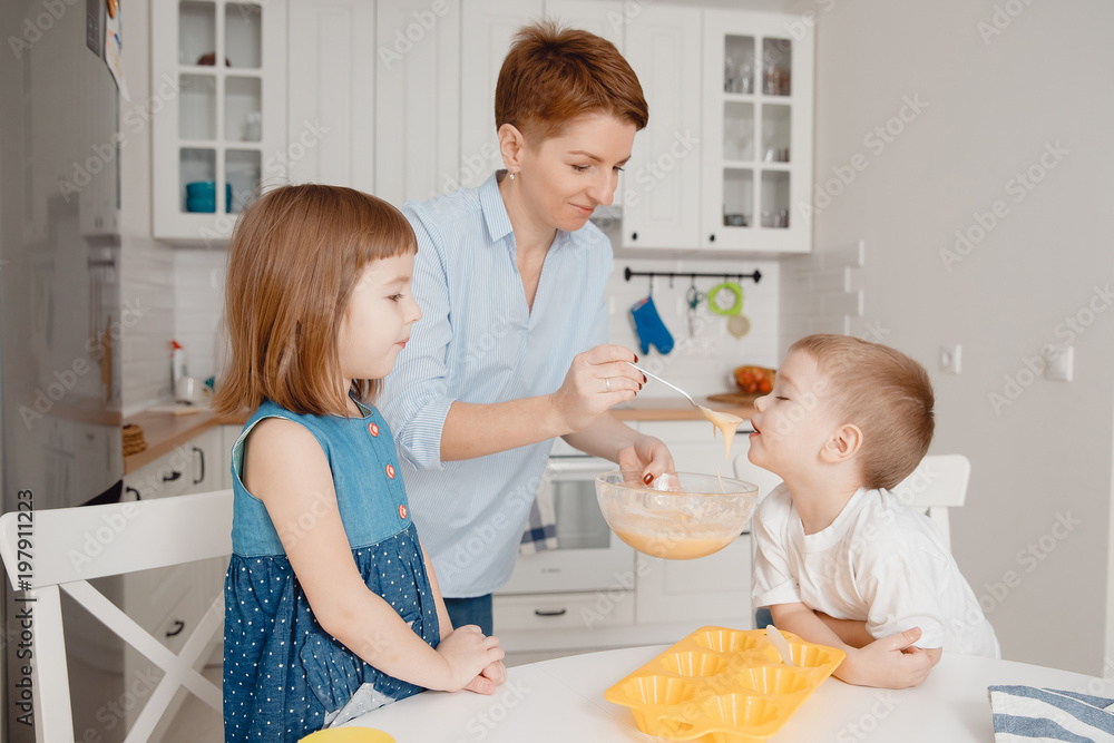 Young family cooking in the kitchen. Happy children with mom, smile, try the dough for baking cupcakes. Young chefs