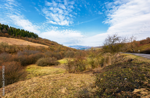 rural fields on mountain slopes in springtime. beautiful countryside scenery by the road. mountain ridge with snowy peak in the distance under the cloudy sky