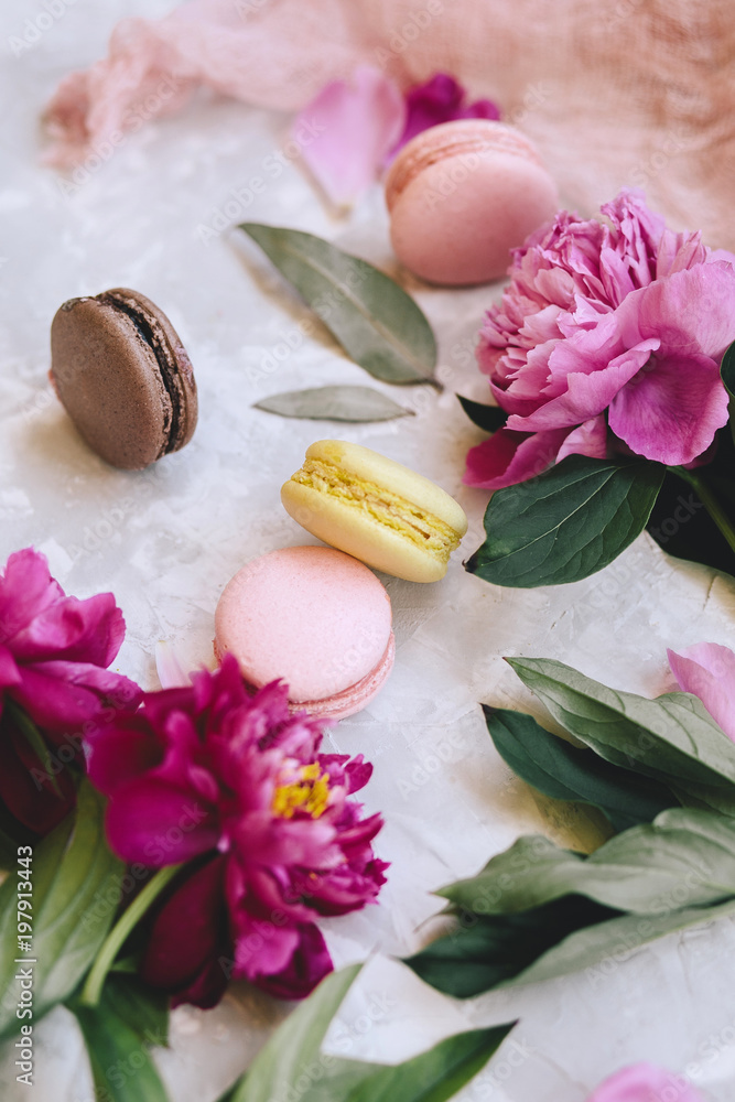 Spring composition: colorful macaroons with purple and pink peonies, green leaves on a light concrete background Spring composition: colorful macaroons with purple and pink peonies, green leaves on a light concrete background