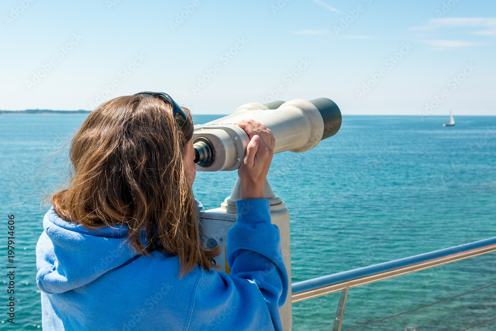 Woman looking through coin operated binoculars at seaside. Woman looking through coin operated binoculars at seaside.