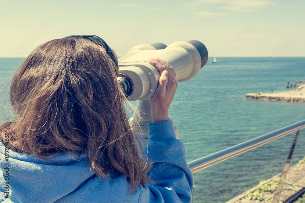Woman looking through coin operated binoculars at seaside. Woman looking through coin operated binoculars at seaside.