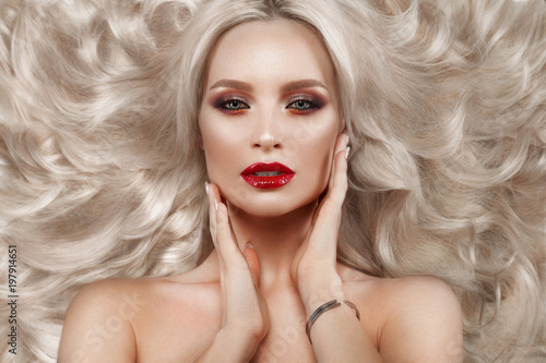 Beautiful blonde in a Hollywood manner with curls, natural makeup and red lips.. Beauty face and hair. Picture taken in the studio