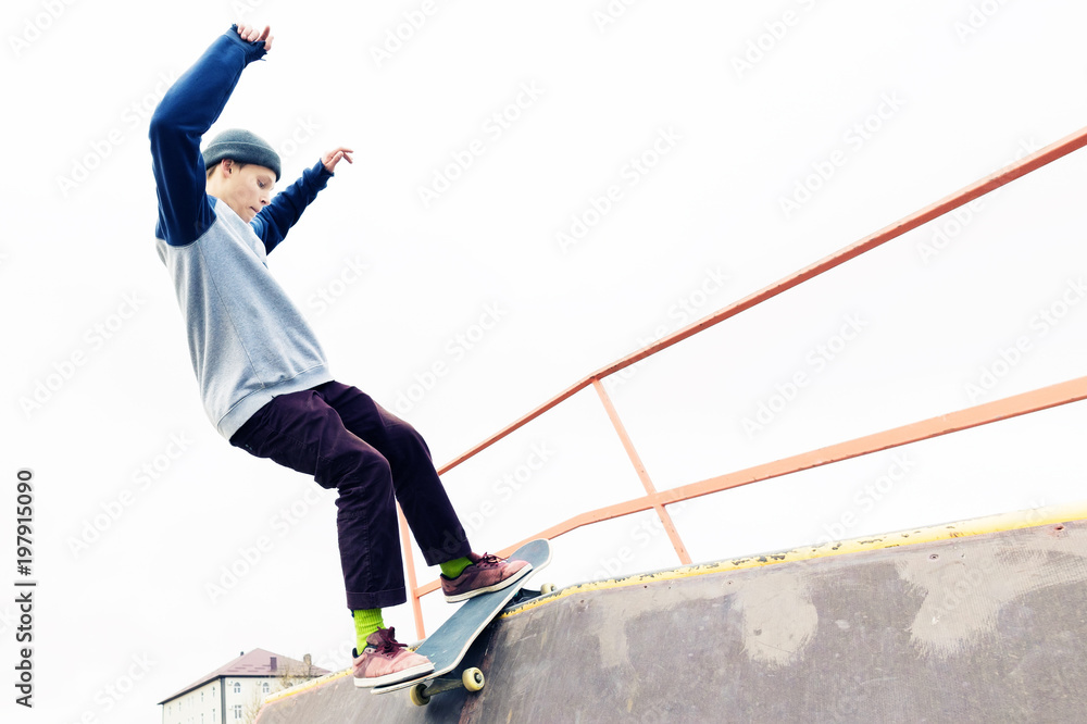 Teen skater in a hoodie sweatshirt and jeans slides over a railing on a skateboard in a skate park