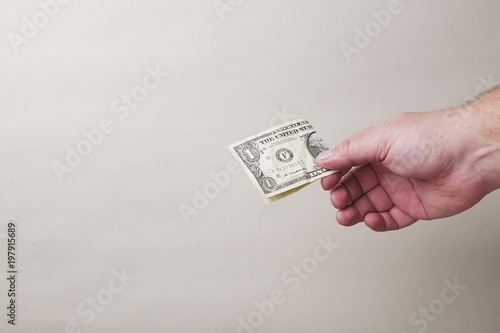 hand giviing one dollar banknote on gray background, copy space