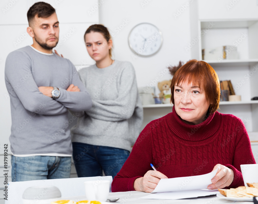 Obraz premium Upset elderly mother with documents, dissatisfied children behind