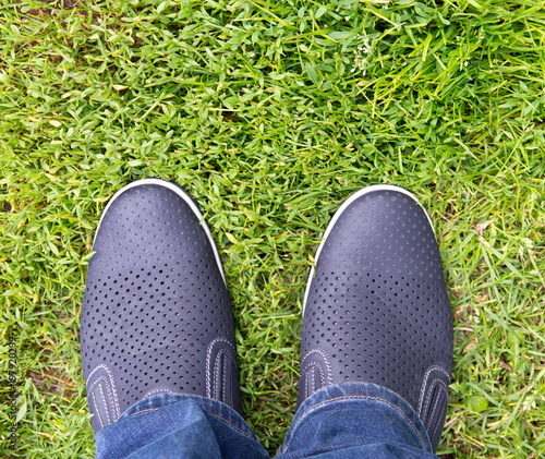 A man in jeans and summer shoes on the background of green grass . Loafers.