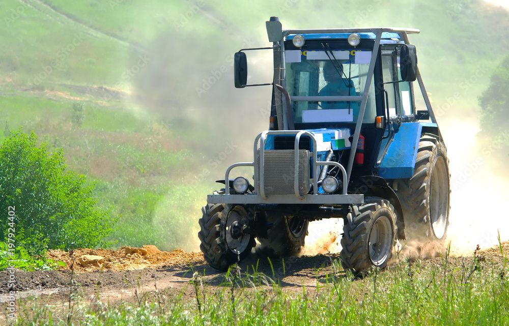 Obraz premium The blue tractor participates in the race. From under the wheels flies dust and stones. The race is in full swing.