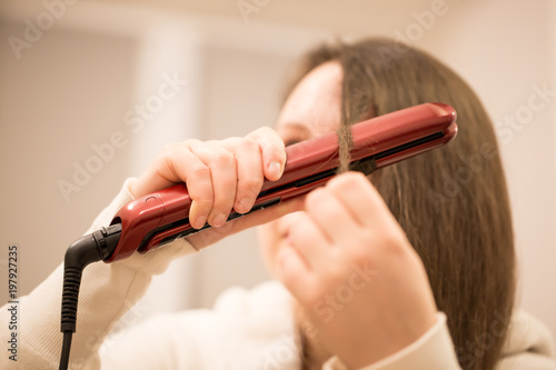 Pretty young brunette woman ironing the hair by professional curling iron