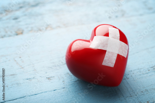 Red heart with adhesive bandage on blue wooden table