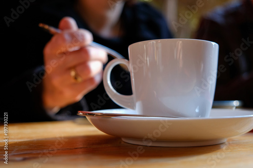 Cup of coffee, with a hand holding a fork in background, afternoon tea