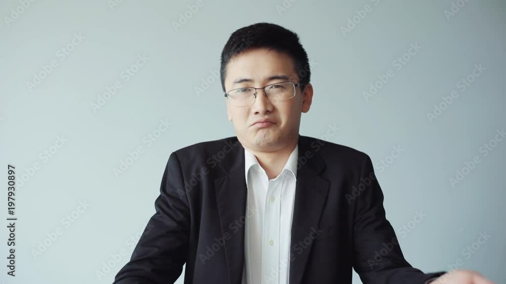 Portrait young chinese officer manager with glasses looks camera in office shrink his shoulders business asian attractive modern handsome businessman face man guy jacket slow motion close up Portrait young chinese officer manager with glasses looks camera in office shrink his shoulders business asian attractive modern handsome businessman face man guy jacket slow motion close up