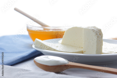 Cheese, honey and sour cream, feta in a white plate, soft cheese on a white background, wooden spoon with sour cream, French breakfast, blue napkin, honey in glassware, blank for designer