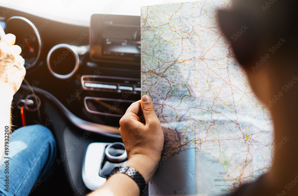 Obraz premium Hipster man holding in male hands and looking on navigation map in auto, tourist traveler hiker driving on background view way road, trip in transportation, person sitting on backdrop window auto