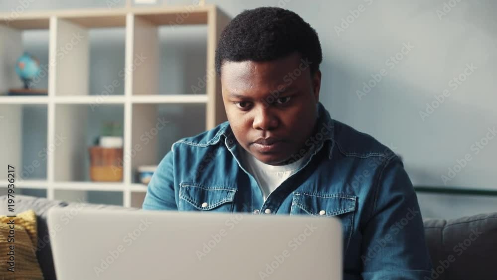 Portrait african american handsome man uses computer for work in home sit on sofa programmer looks at monitor screen freelance successful worker businessman engineering Slow motion Portrait african american handsome man uses computer for work in home sit on sofa programmer looks at monitor screen freelance successful worker businessman engineering Slow motion