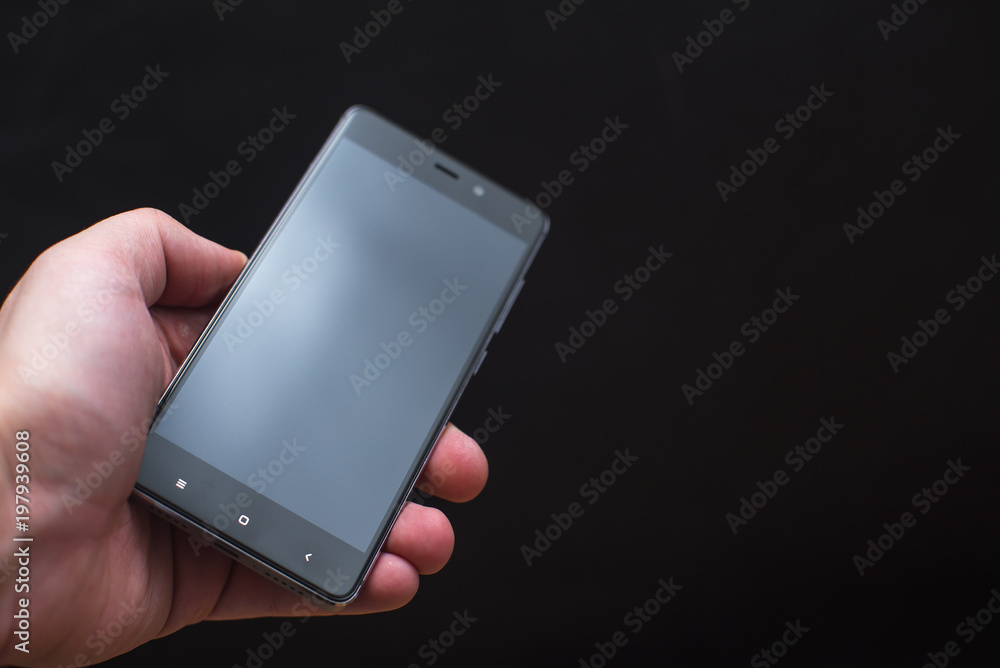 Hand holding black smartphone isolated on black background Hand holding black smartphone isolated on black background