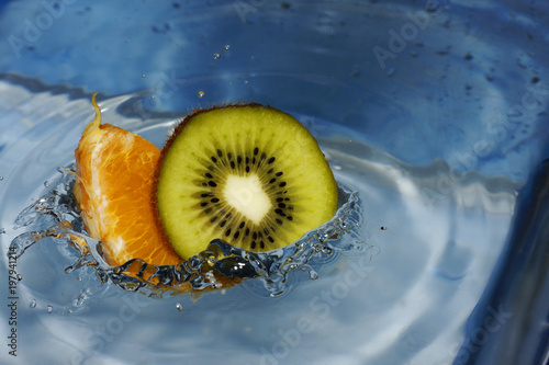 Falling kiwi and orange fruit into the water with a beautiful splash.
