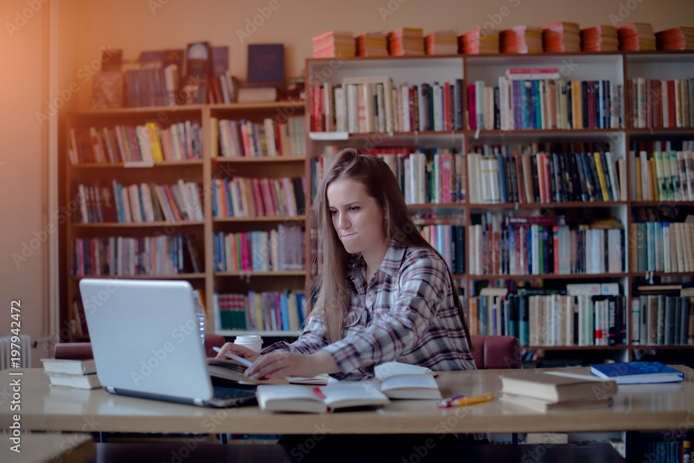 Focused young woman working on laptop in library Focused young woman working on laptop in library