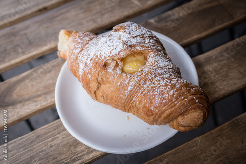Bild auf Leinwand Piattino con cornetto alla crema su un tavolo a doghe di legno