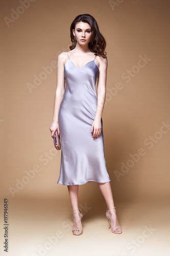 Sexy beauty woman pretty face tan skin wear lilac silk dress long skinny body shape makeup cosmetic summer collection studio catalog brunette curly hair clothes for date meeting walk party fashion.