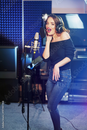 Young female singer recording album in the professional studio. Woman singing a song in music recording studio.