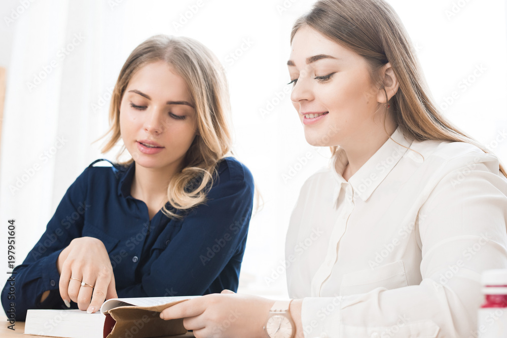 Female students sitting together at the table and reading a book Female students sitting together at the table and reading a book