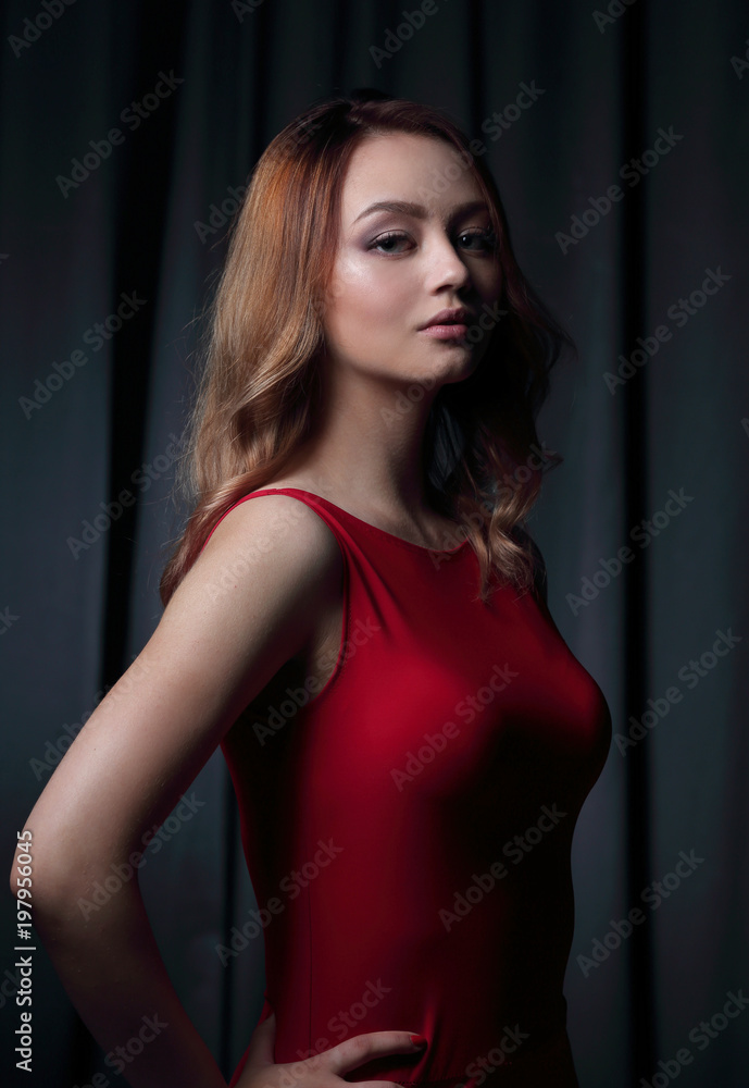 Fototapeta premium Charming brunette in a red dress posing on a black background.