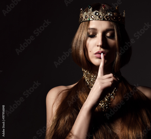 Beautiful sexy brunette beauty woman with long hair wear gold crown and jewellery show tsss sign on dark  photo