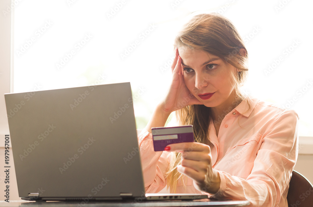Young blond Caucasian woman worried to pay electronic bills, with several credit cards in hand. Young blond Caucasian woman worried to pay electronic bills, with several credit cards in hand.