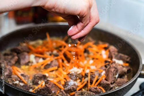 Hand adds salt to beef stew close