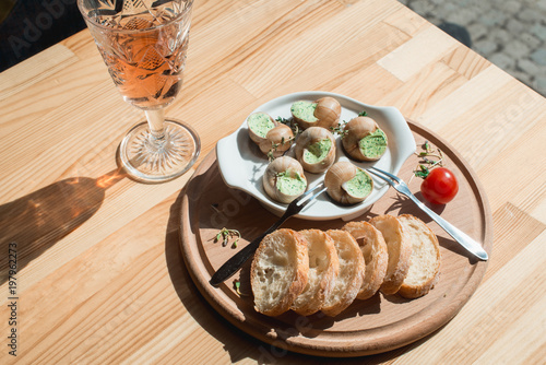 Snails with herbs butter, in traditional ceramic pan bread on a wooden plank. Glass of wine