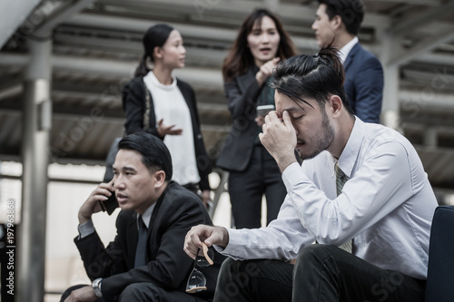 Businesspeople Gossiping Behind Stressed business man.