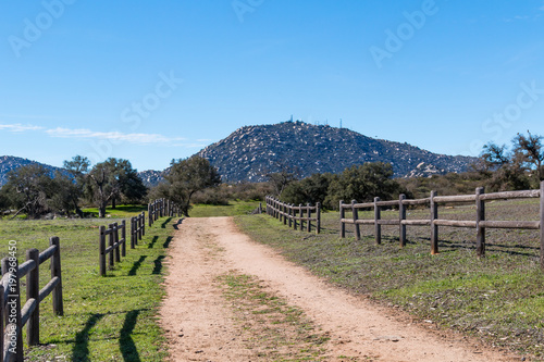 A dirt road lined with a wooden fence leading to Mount Woodson at Ramona Grasslands Preserve in San Diego, California.