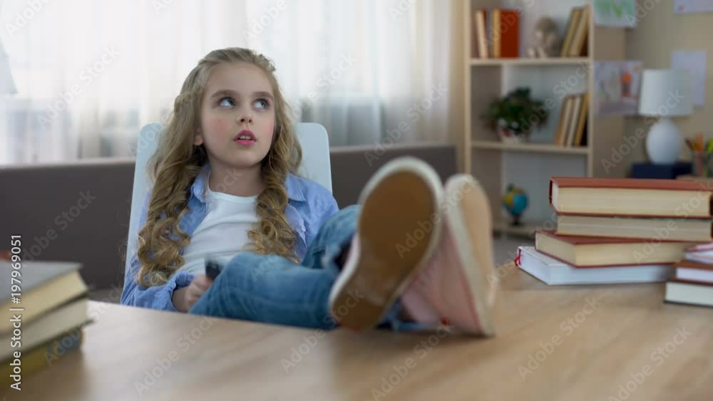 Smiling child sitting at table and playing game on smartphone, gadget addiction Smiling child sitting at table and playing game on smartphone, gadget addiction