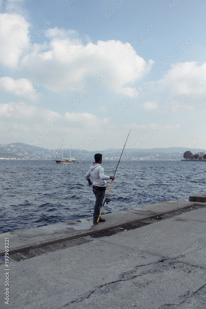 Fisherman by Bosphorus strait in Tarabya area of Istanbul. Wooden yacht is in the background.