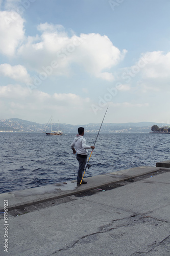Fisherman by Bosphorus strait in Tarabya area of Istanbul. Wooden yacht is in the background.