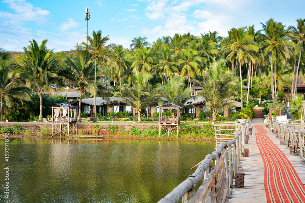 The river on the beach in Mandrem overlooks buildings and a wooden bridge on stilts with a carpet in North Goa.India
