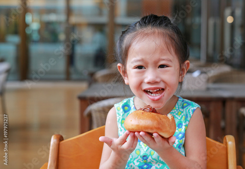 Smiling little Asian girl eating bread. Asian girl having breakfast.