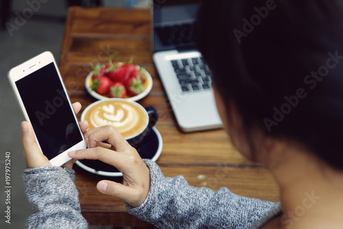 Close up view on the hands of a young woman holding a smartphone tapping the blank screen. Girl using device in a cafe.