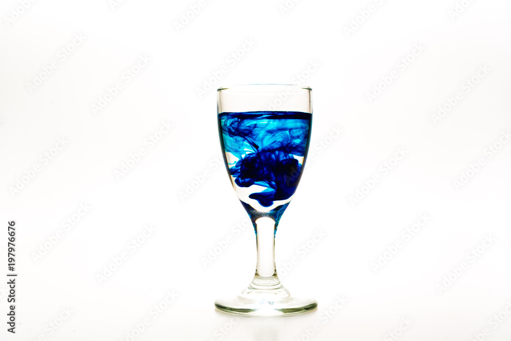 Blue food coloring diffuse in water inside wine glass with empty copy-space area for slogan or advertising text message, over isolated white background. Blue food coloring diffuse in water inside wine glass with empty copy-space area for slogan or advertising text message, over isolated white background.