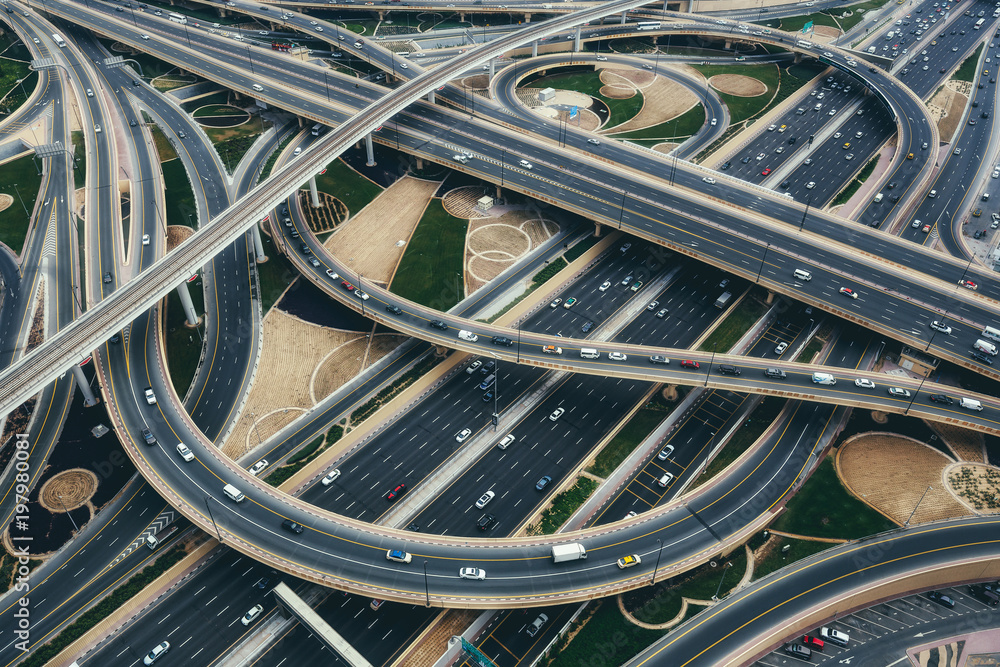 Obraz premium Widok z lotu ptaka na duże skrzyżowanie autostrad z ruchem w Dubaju, ZEA, w dzień. Malowniczy pejzaż. Kolorowe tło transportu, komunikacji i jazdy.