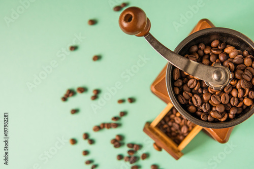 Coffee beans in a hand-held coffee grinder on a tender green background top view