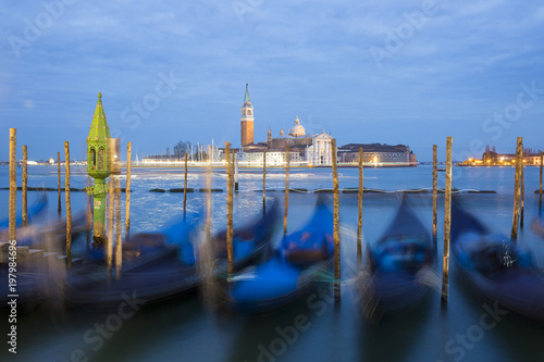 Romantic colorful night view on the lagoon of Venice at sunset during blue hour with moving gondolas and San Giorgio Maggiore church and campanile in the background © Melanie