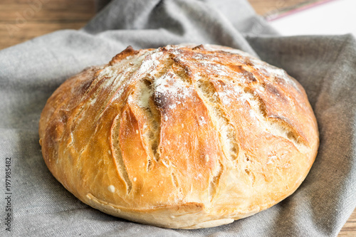 Freshly baked round, uncut bread on grey kitchen table cloth.