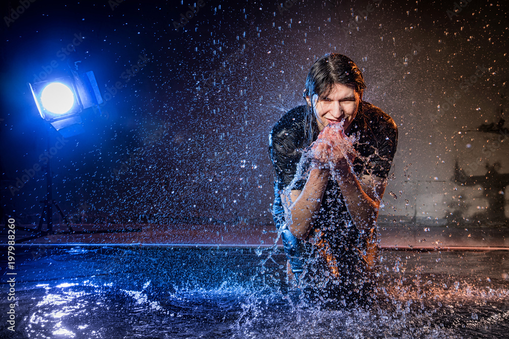 Attractive young man in black wet clothes under the rain and splash of water, studio photo Attractive young man in black wet clothes under the rain and splash of water, studio photo