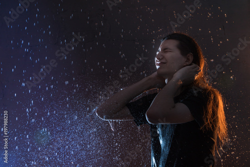 Attractive young man in black wet clothes under the rain and splash of water  studio photo