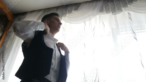 a bridegroom prepares for a wedding and dresses his vest and jacket in black and white. a future husband closes the button on his jacket for the wedding. photo