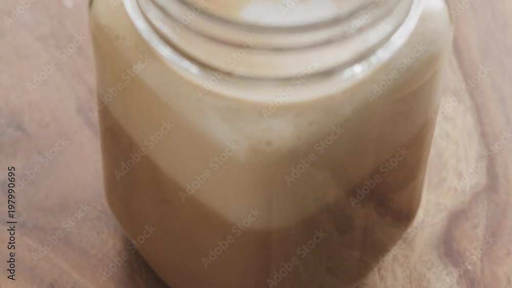 Slow motion making coffee drink in glass jar with handle on wood table, adding straw Slow motion making coffee drink in glass jar with handle on wood table, adding straw