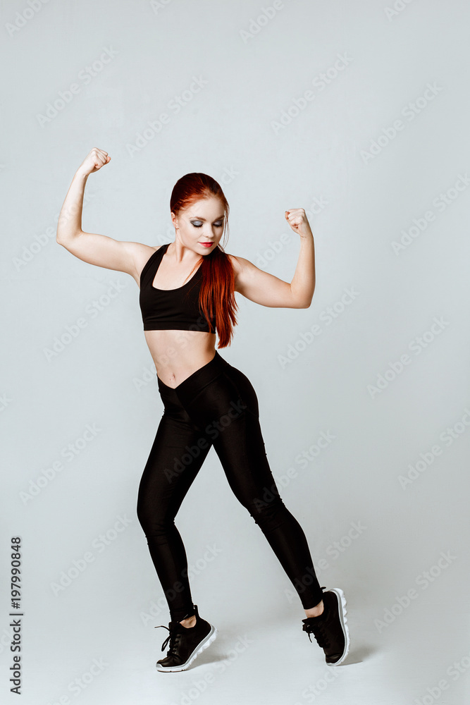 fitness and training concept.Nice red-haired young woman in sportswear poses  isolated over white background.girl shows us bicepses, strong hands. 