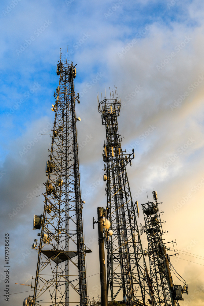 Low angle view of telecommunications towers against cloudy sky Low angle view of telecommunications towers against cloudy sky